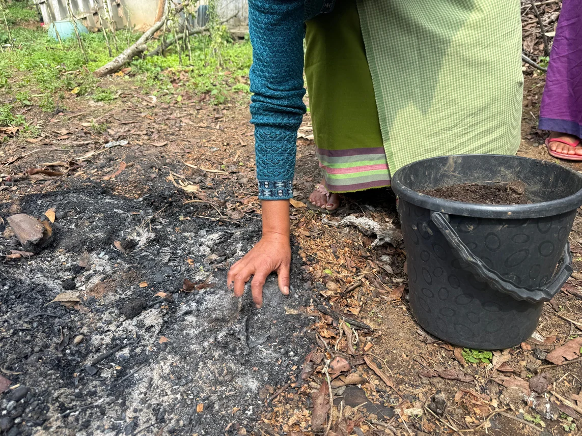 Kitchen ash and biochar being collected by hand from a hearth